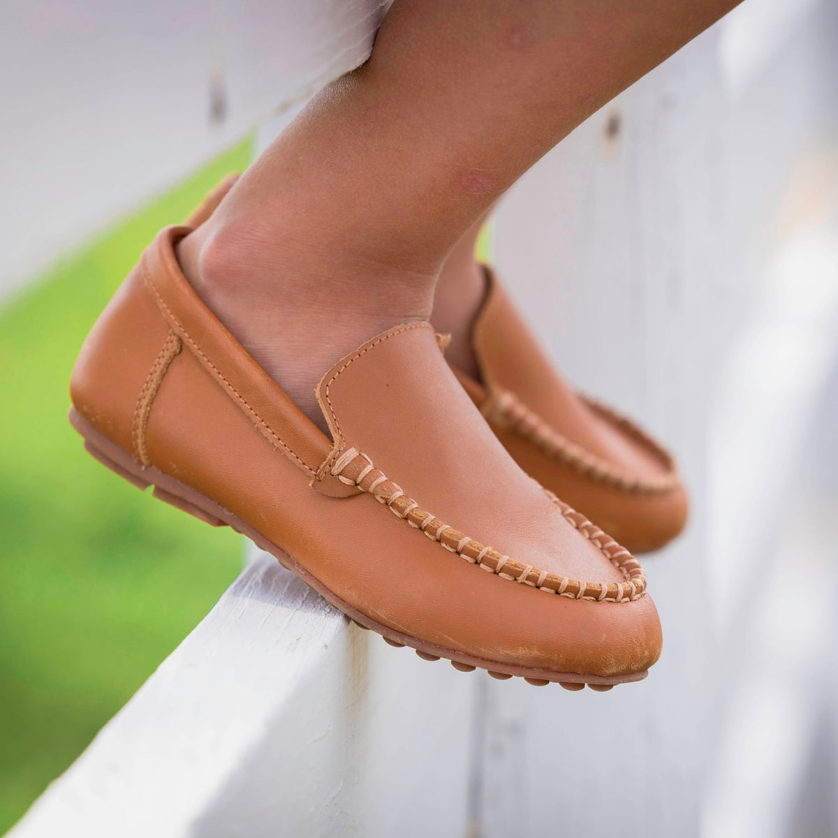 Caramel leather loafers worn on a white fence