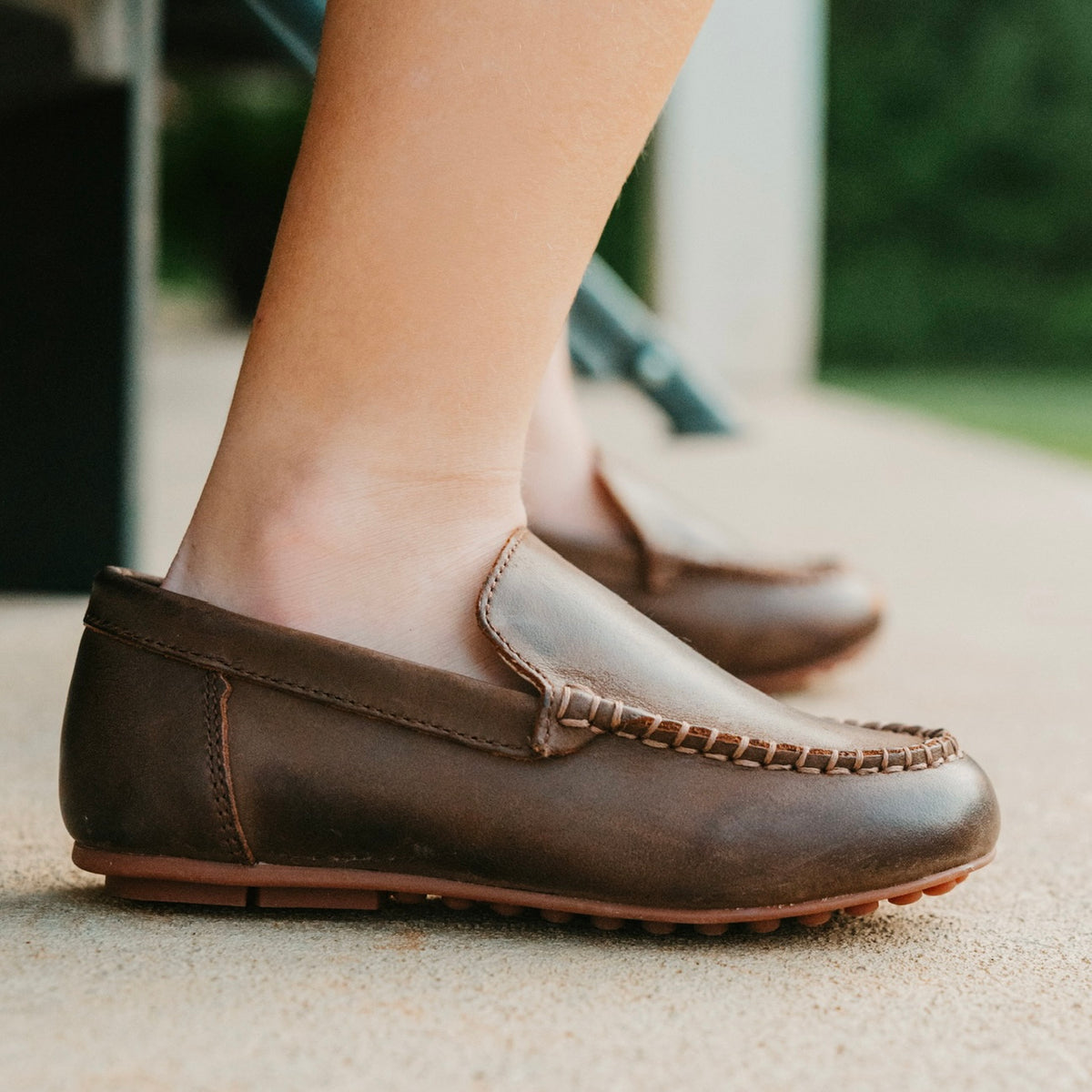 Chocolate leather loafers worn on a porch.