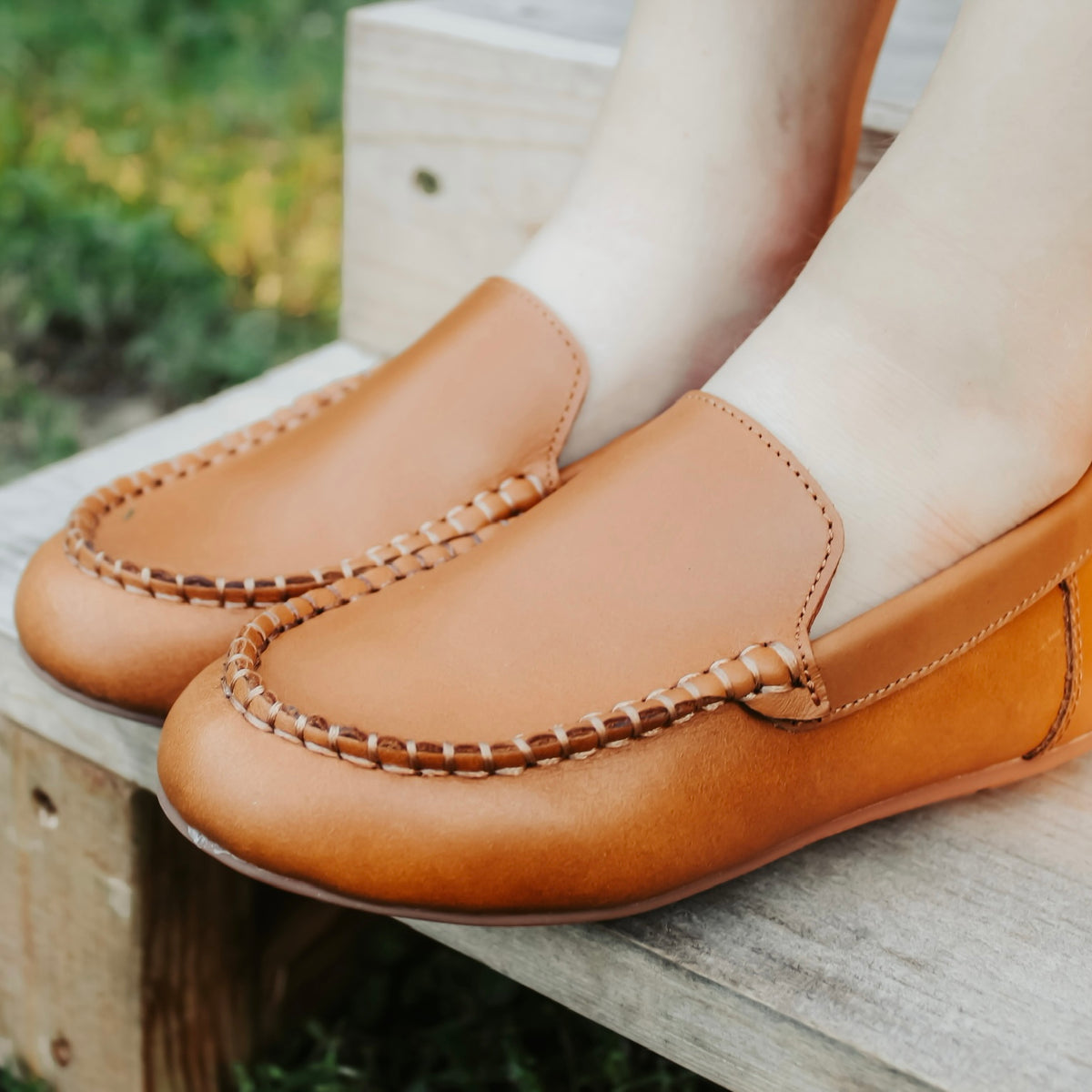 Caramel leather loafers worn on a wooden bench.