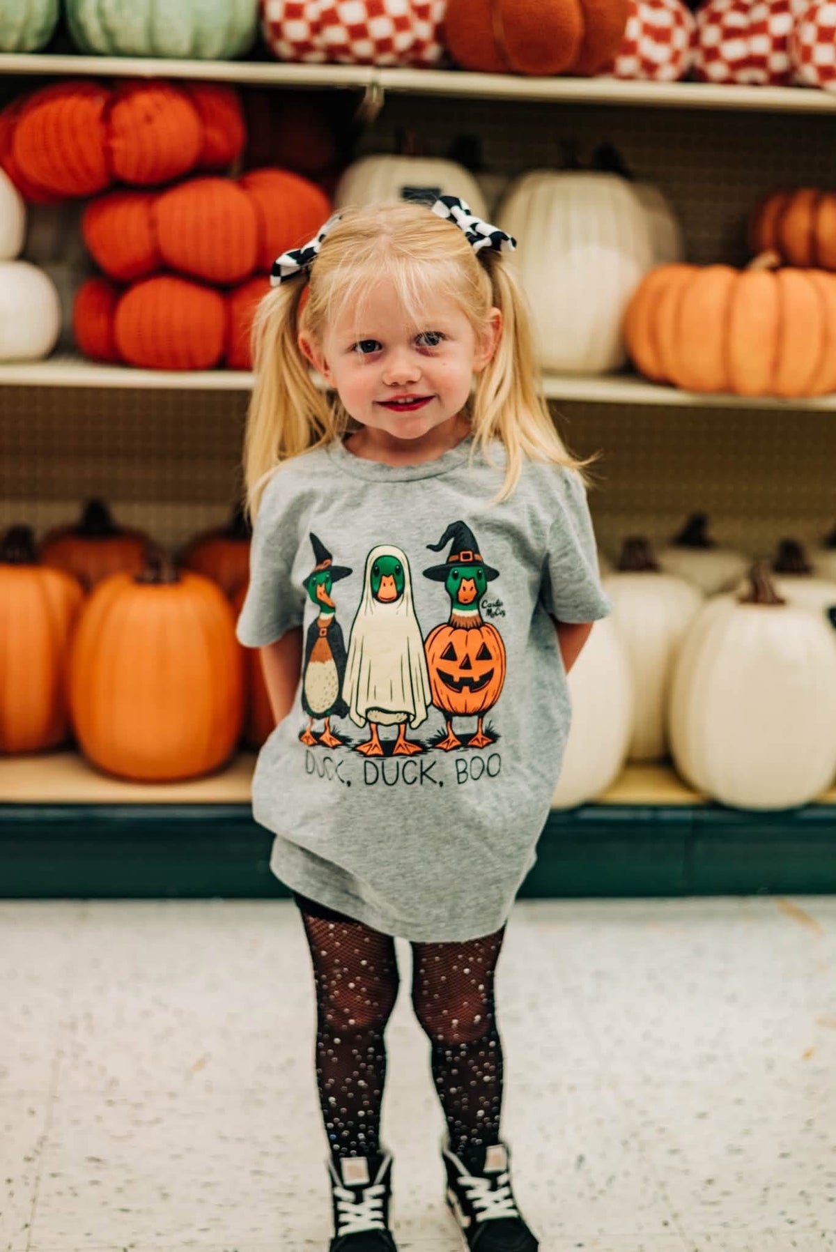 A child wearing a Duck, Duck, Boo front graphic tee beside pumpkins.