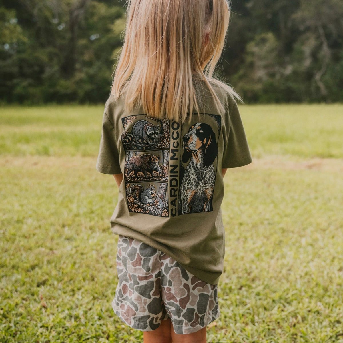 A child wearing a Cardin McCoy hunting dog graphic tee outdoors.