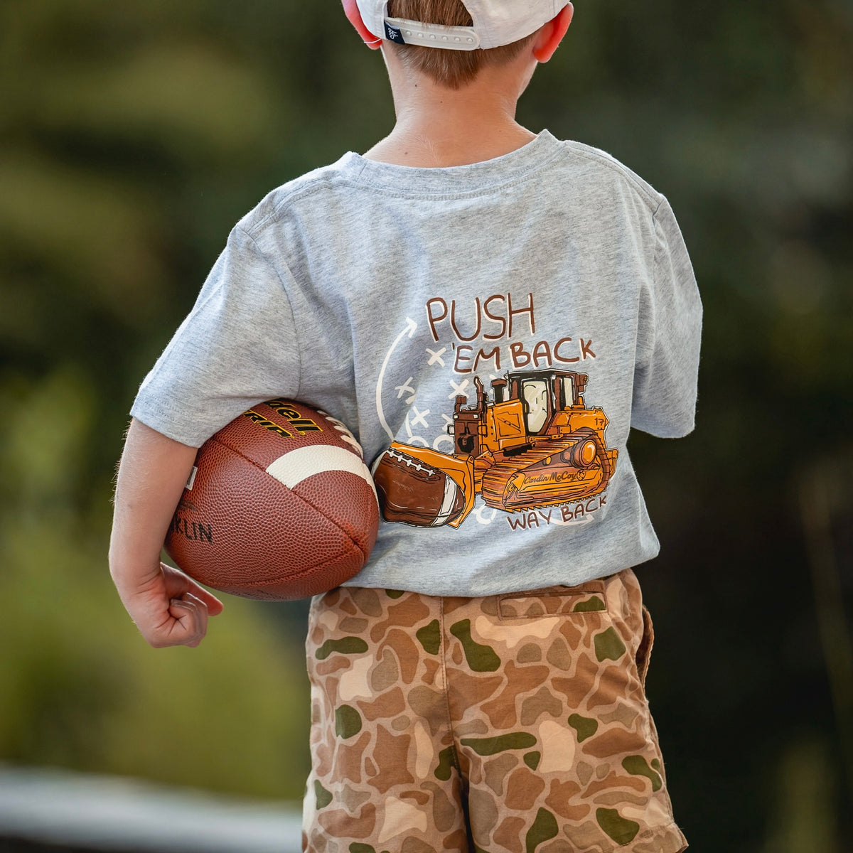 A child wearing camo shorts while holding a football.